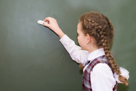 girl in school uniform writes with chalk on blackboardの写真素材