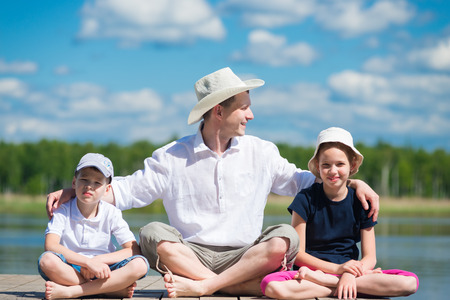 father with daughter and son sits on a beautiful pier on the lakeの写真素材