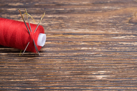 Red thread with a needle on a wooden table