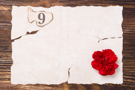Burnt piece of paper on the table, with a red carnation and the number 9の写真素材