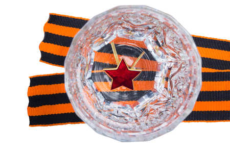 Red star on the bottom of a faceted glass in Russian vodka, to the day of victory, stands on a St. George ribbon, on an isolated white backgroundの写真素材