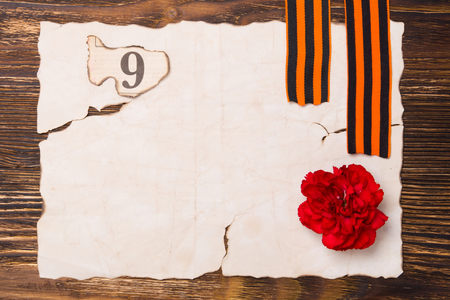 A burnt sheet of paper on the table, with a red carnation and a number 9, and two St. George ribbonsの写真素材