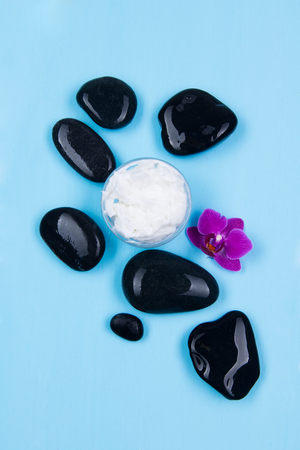 Cream with the smell of orchids surrounded by black stones on a blue backgroundの写真素材