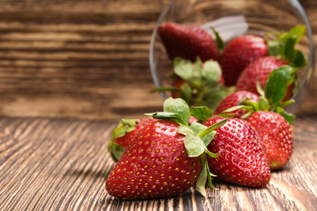 red strawberries dropped from a bowl on a dark boardの写真素材