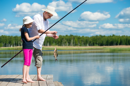 Dad and daughter caught a fish in a bait in the lakeの写真素材