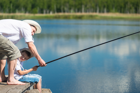 Dad with his son on the river caught a fish on a fishing poleの写真素材