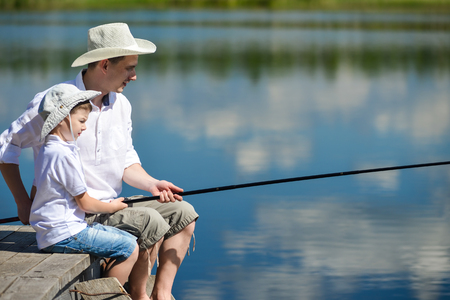 Dad and son are sitting on the pier and fishing on the riverの写真素材