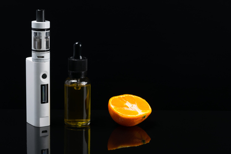 White electronic cigarette on a black background, next to the mandorin gum for fillingの写真素材