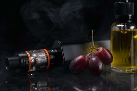 Electronic cigarette and grapes with a bottle of liquid in the smoke on a black backgroundの写真素材