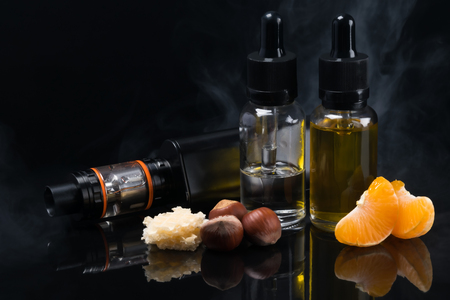 Electronic cigarette with different flavors in bottles with reflection on a black backgroundの写真素材