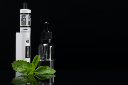 E-cigarette with reflection on a black background next to mint leavesの写真素材