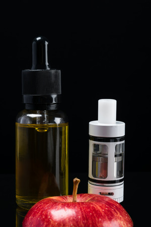 Electronic cigarette and liquid with a taste of a red apple on a black backgroundの写真素材