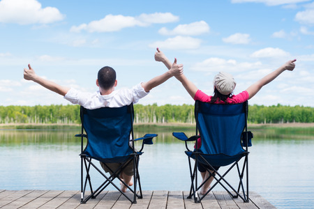Man and woman are sitting on chairs and enjoying the beautiful nature of the lakeの写真素材