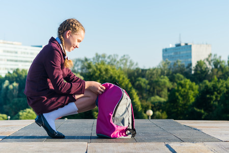 Girl in a school uniform opens a pink backpack for textbooks