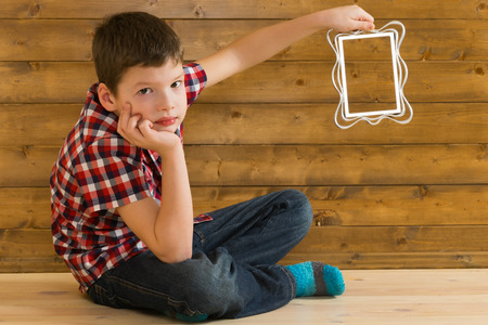 Boy holds a photo frame on the background of a wooden wallの写真素材