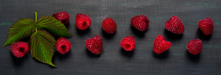 Red raspberry lies on a black background, along with a green leafの写真素材