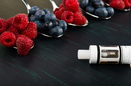 Background of berries in spoons of raspberries and blueberries, next to an electronic cigarette on a black backgroundの写真素材