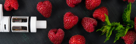 a white electronic cigarette, on a black painted board, next to a green mint, and a red raspberryの写真素材