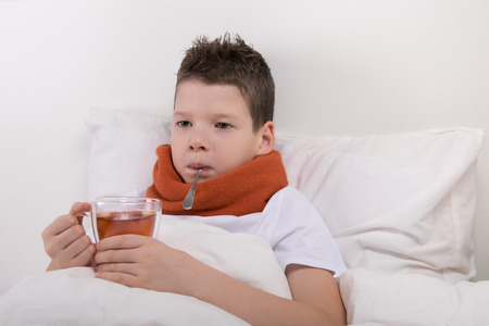 a sick boy drinks warm tea without getting out of bedの写真素材