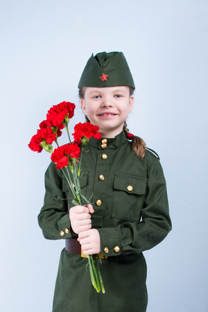 child girl standing in uniform with red flowers on a blue backgroundの写真素材