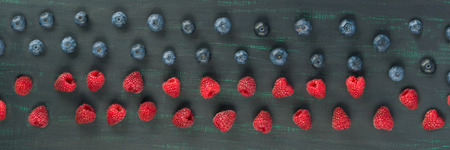 red raspberries and blueberries lie on a dark background, long photoの写真素材