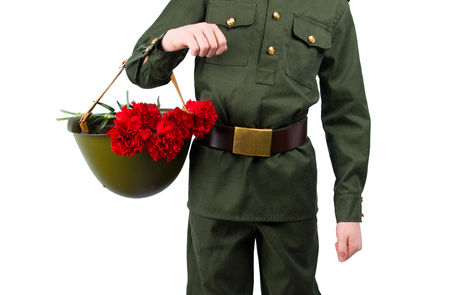 child in military uniform, holding in his hand a hard hat with carnations, on a white backgroundの写真素材