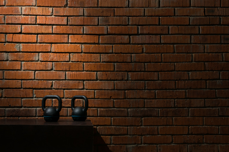 two black dumbbells for sport in a dark room against a brick wall backgroundの写真素材