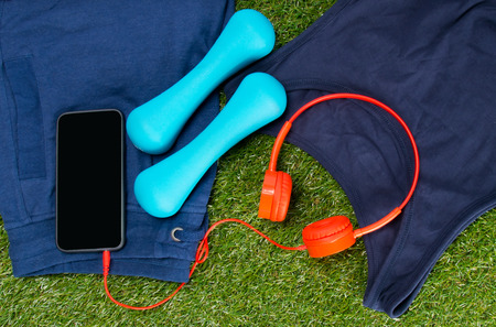 blue sportswear, dumbbells for fitness and a mobile phone with red headphones, against the background of grassの写真素材