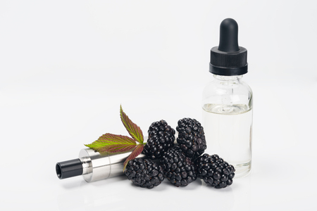 electronic cigarette and concentrate for it in a bottle with a blackberry taste next to a berry on a white backgroundの写真素材