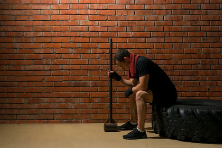 athlete sits on a rubber wheel for exercising, against a brick wall backgroundの写真素材