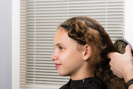 The hairdresser's hands prepare the girl's long hair for a haircut