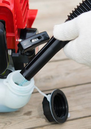 a lawn maintenance worker, refills blue fuel chainsaw, on a wooden background.