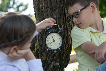 girl with a boy-schoolchildren, watch the arrows on the clock, in the open airの写真素材