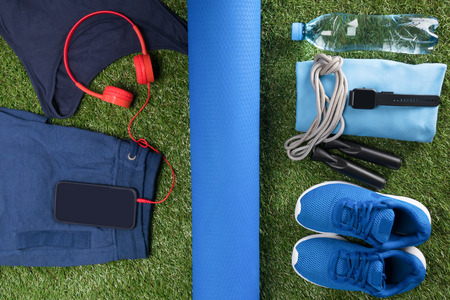on a green lawn, a set of blue sports things and shoes, a black phone with red headphones for listening to musicの写真素材