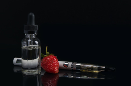 electronic cigarette and liquid for it, with a taste of strawberries, on a black backgroundの写真素材