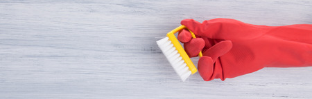 on a light background, a hand in a red glove, holds a brush for cleaning, there is a place for an...