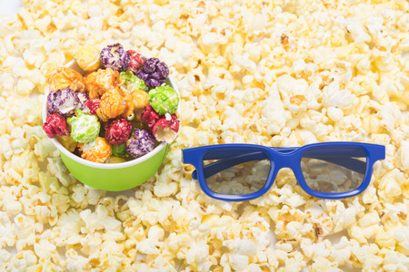 3-D glasses and paper cup with multi-colored popcorn on the background of scattered ready-made corn kernelsの写真素材