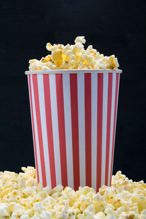 a red-white paper cup with ready-made corn kernels on a black background stands on popcornの写真素材