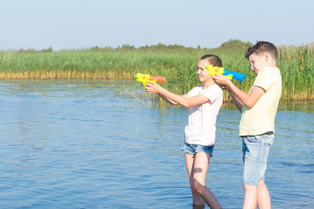 boy and girl play with water pistols on the riverの写真素材