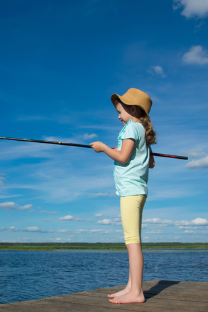 girl in a hat, against the blue sky with clouds, fishing, standing on the pierの写真素材