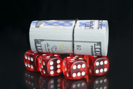 a bundle of hundred dollar bills, on red dice, on a black background, with reflectionの写真素材
