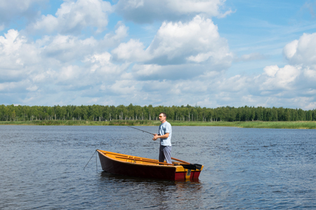 a man standing in a boat fishing for fishing on a lake in the forestの写真素材