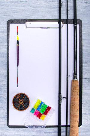 tablet with a white sheet of paper, on a light gray table, with items for fishing, fishing pole, floats, sinkers and bait, there is a place for an inscriptionの写真素材