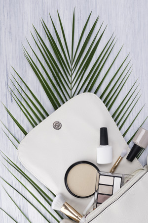 White small women's handbag and makeup cosmetics are on the background of a green twig.の写真素材