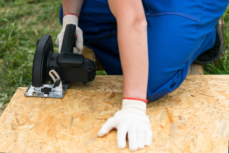 worker's hands hold a circular saw to cut a wooden shield