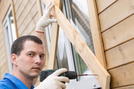 the owner of the house in the village unscrews the screws with a screwdriver from the boards and...