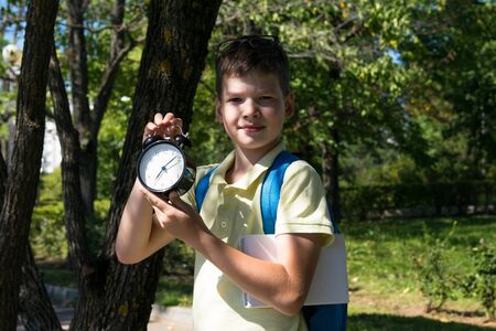 student in the park keeps an alarm clock, time back to school, holidays are overの写真素材