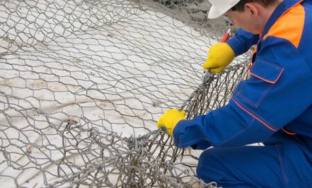 worker in blue uniform and white helmet repairing mesh for dirt stones, close-up