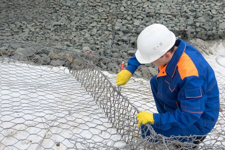 a worker in a helmet at a construction site knits a foundation from a wire