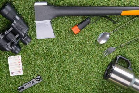on a green lawn, a set of tourist, mug, fork, spoon, knife, thermos, ax, binoculars, lantern, matches, in the middle there is a place for an inscriptionの写真素材